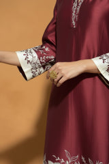 Maroon traditional outfit with floral cuffs and a gold ring on a brown background