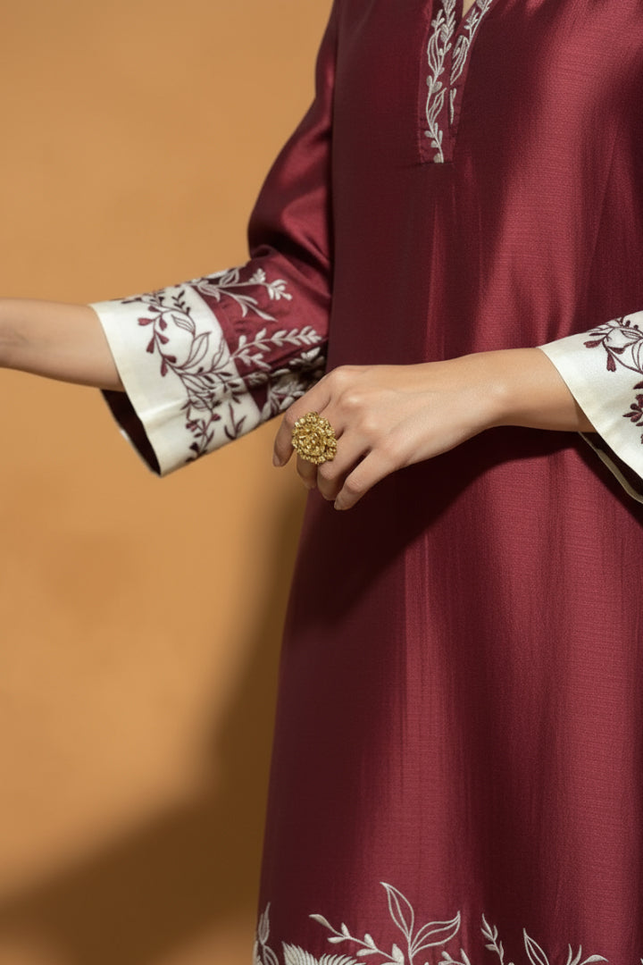 Maroon traditional outfit with floral cuffs and a gold ring on a brown background